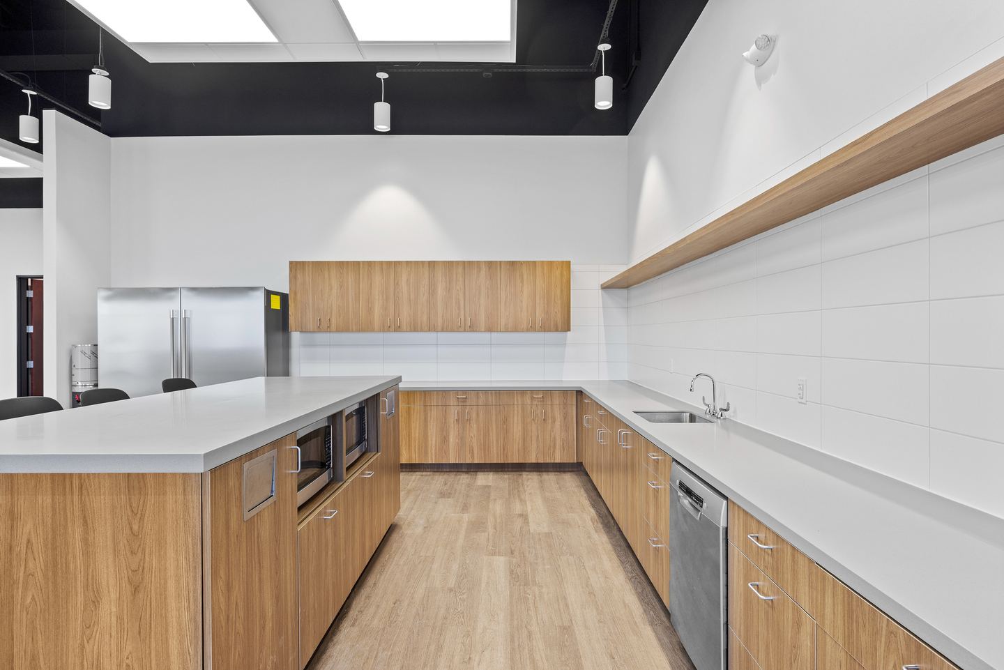 Office staff kitchen with wood cabinetry, a white island, a long counter run and a stainless refrigerator