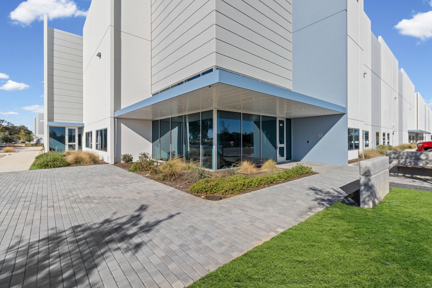 Modern office and warehouse building with a glazed corner entrance, landscaping and a paver walk