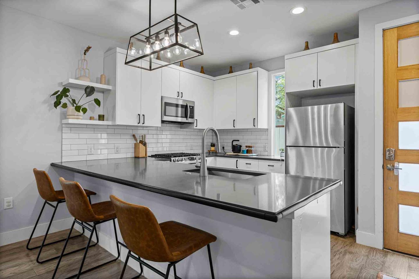 Condo kitchen in Austin with white cabinetry, a waterfall island and bar stools