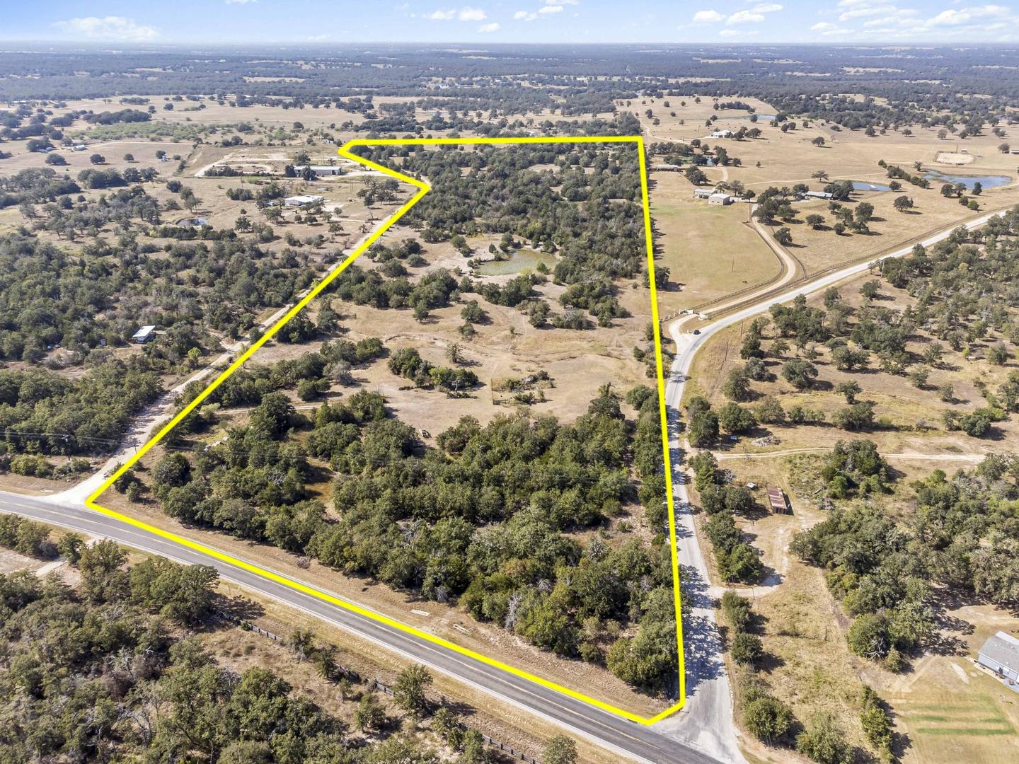 Aerial photograph of a Hill Country parcel with the lot boundary drawn on in yellow over the trees and road frontage
