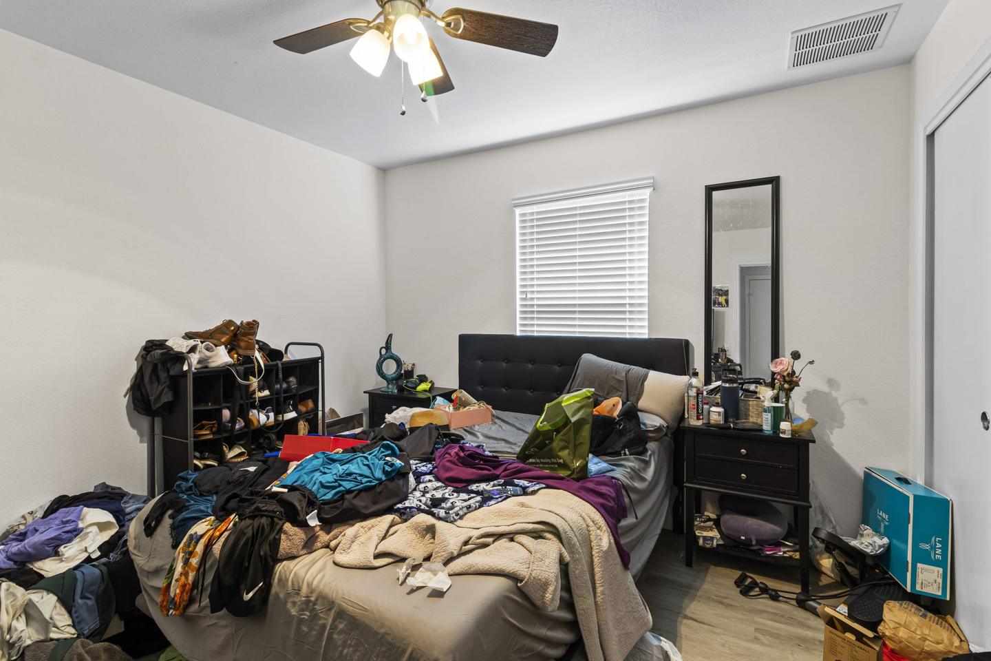 Bedroom crowded with clothes, boxes and furniture stacked against every wall