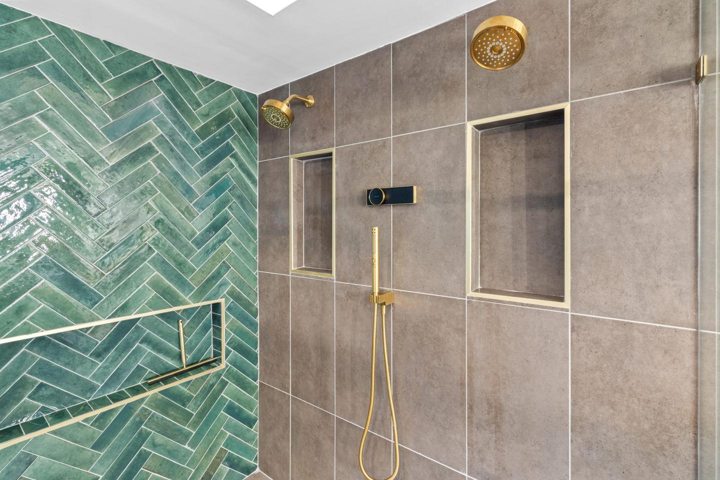 Walk in shower lined in green herringbone tile with brushed gold fittings