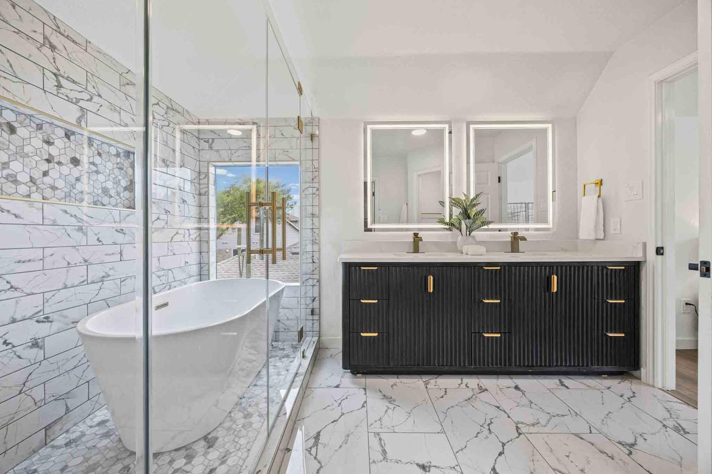 Marble lined bathroom with a freestanding tub, a black double vanity and a glass shower