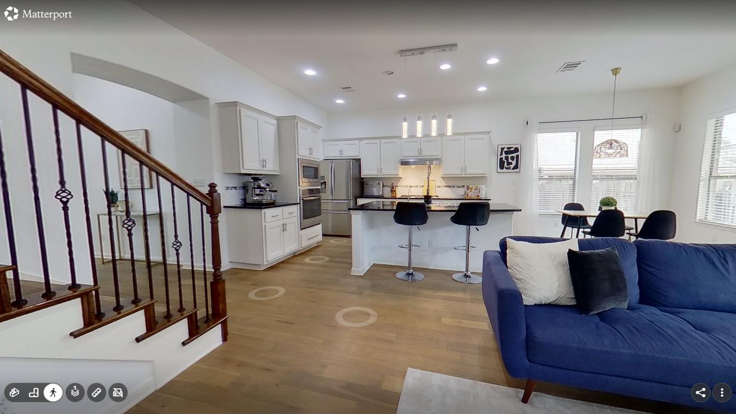 Matterport walkthrough view from a living room toward the kitchen and stairs, with circular markers on the floor showing where the buyer can step next