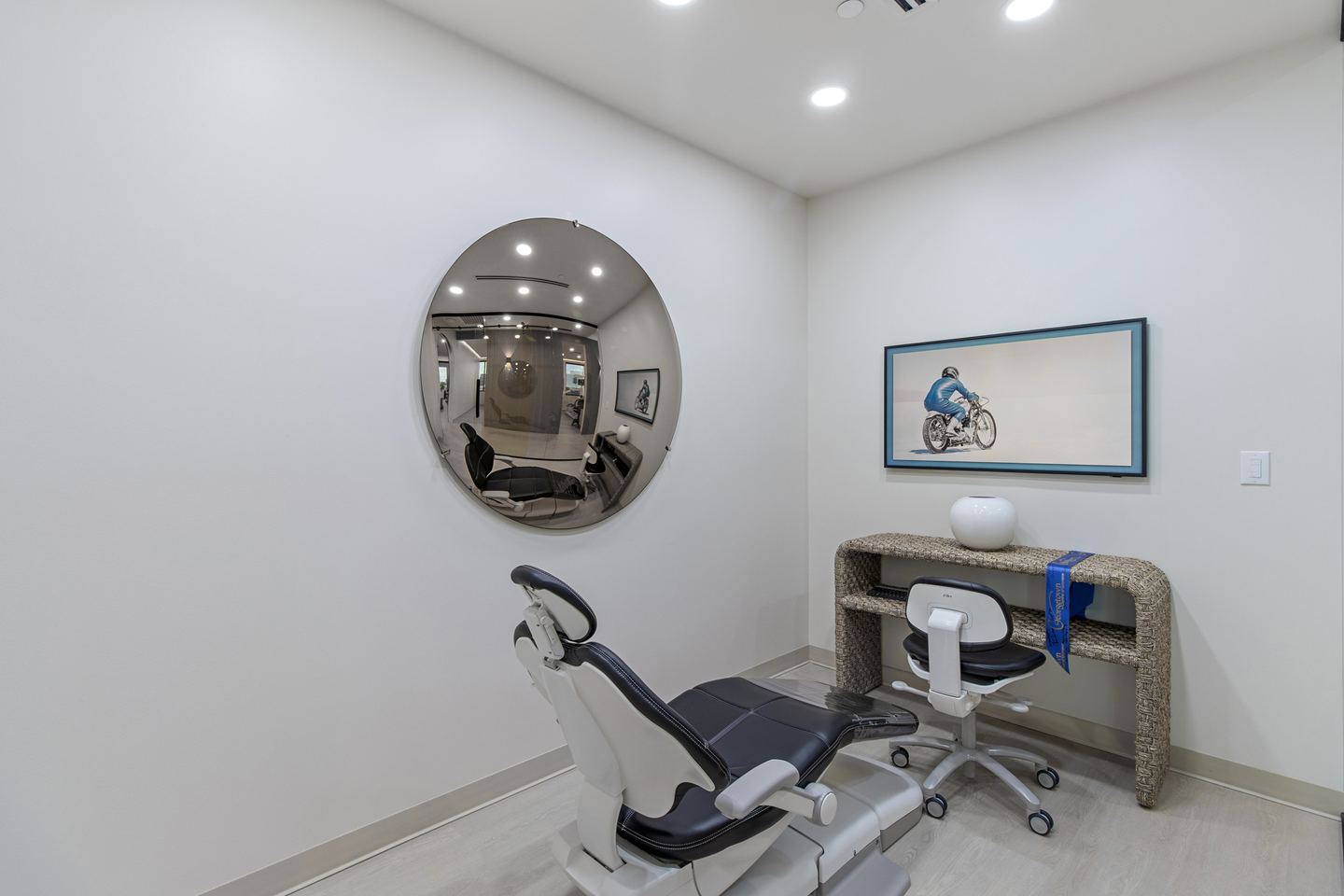 Small consult room with a dental chair, a round convex mirror and a rattan desk