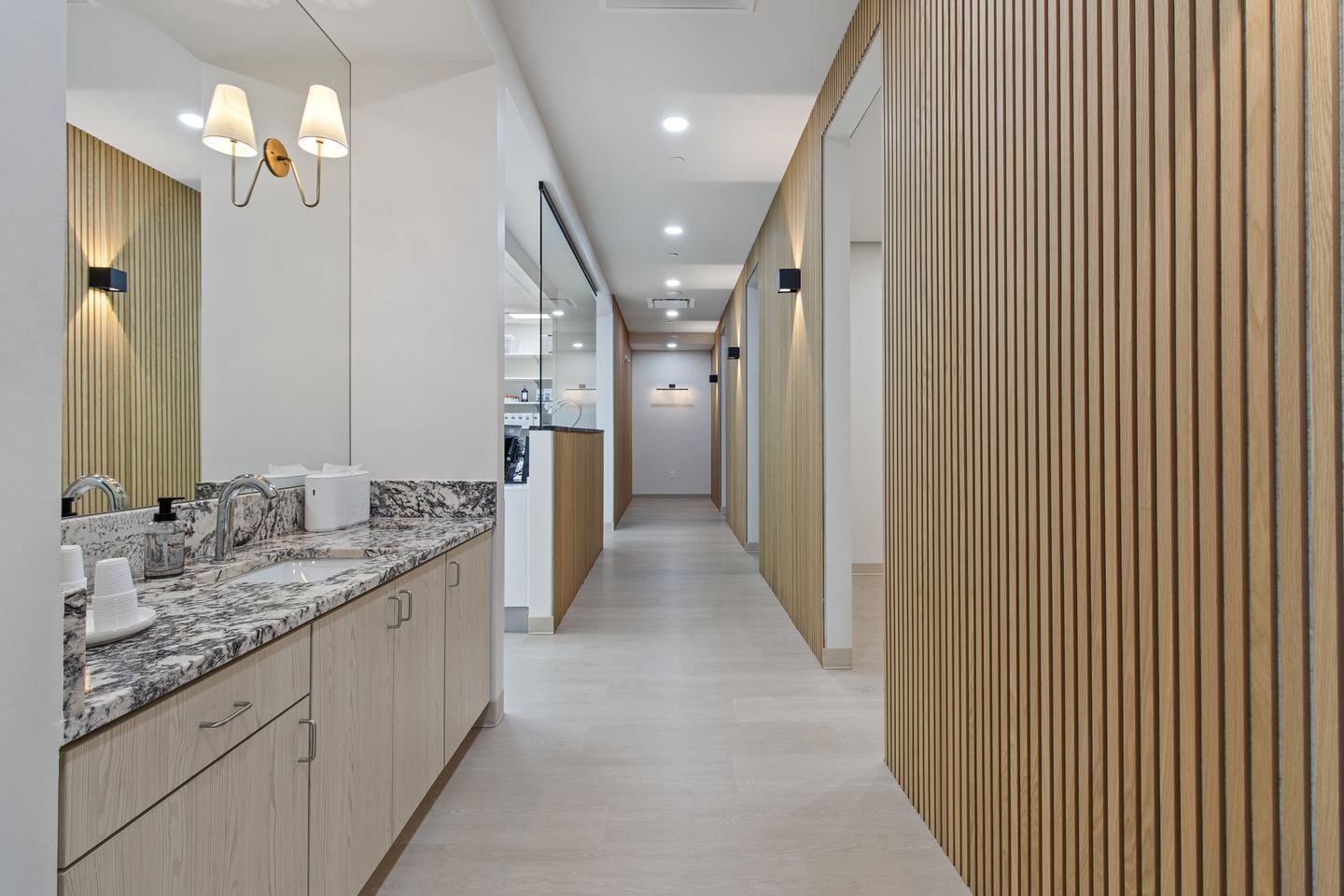 Clinic corridor with a granite vanity, brass wall sconces and a timber slat screen