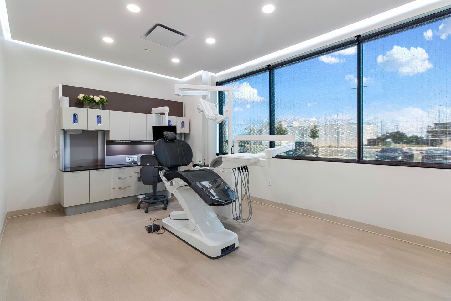 Bright operatory with a full width window, a white dental chair and wall cabinetry