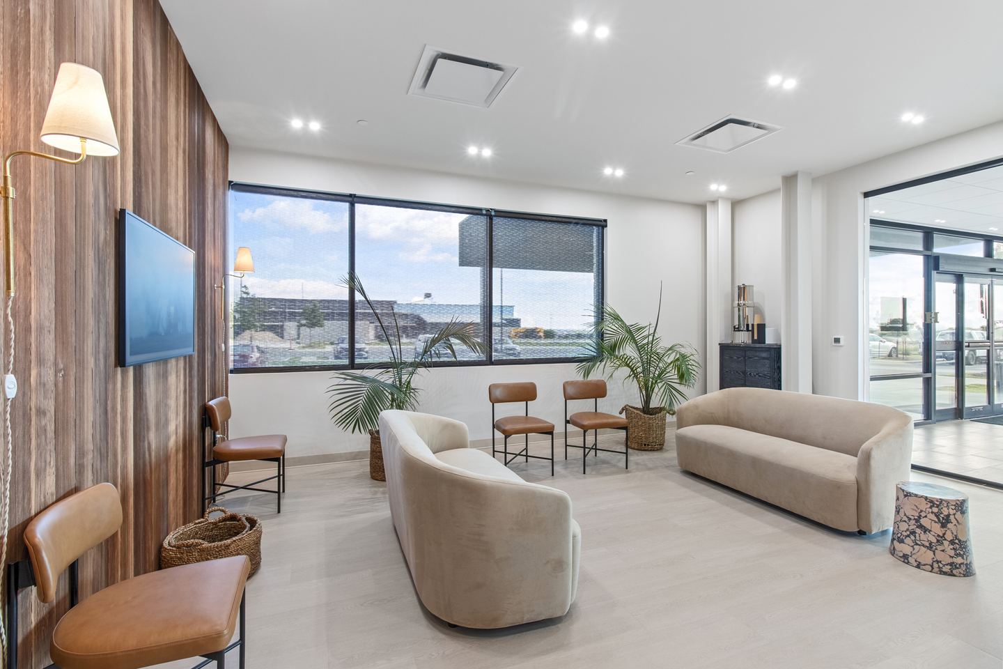 Patient waiting lounge with curved cream sofas, leather chairs and a wall of windows onto the street