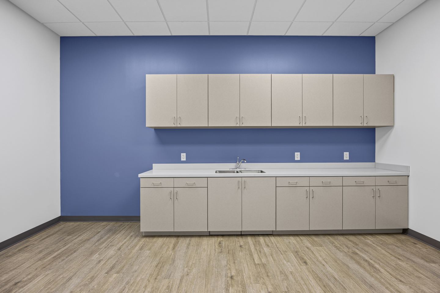 Break room with a blue accent wall, taupe cabinetry and a sink run