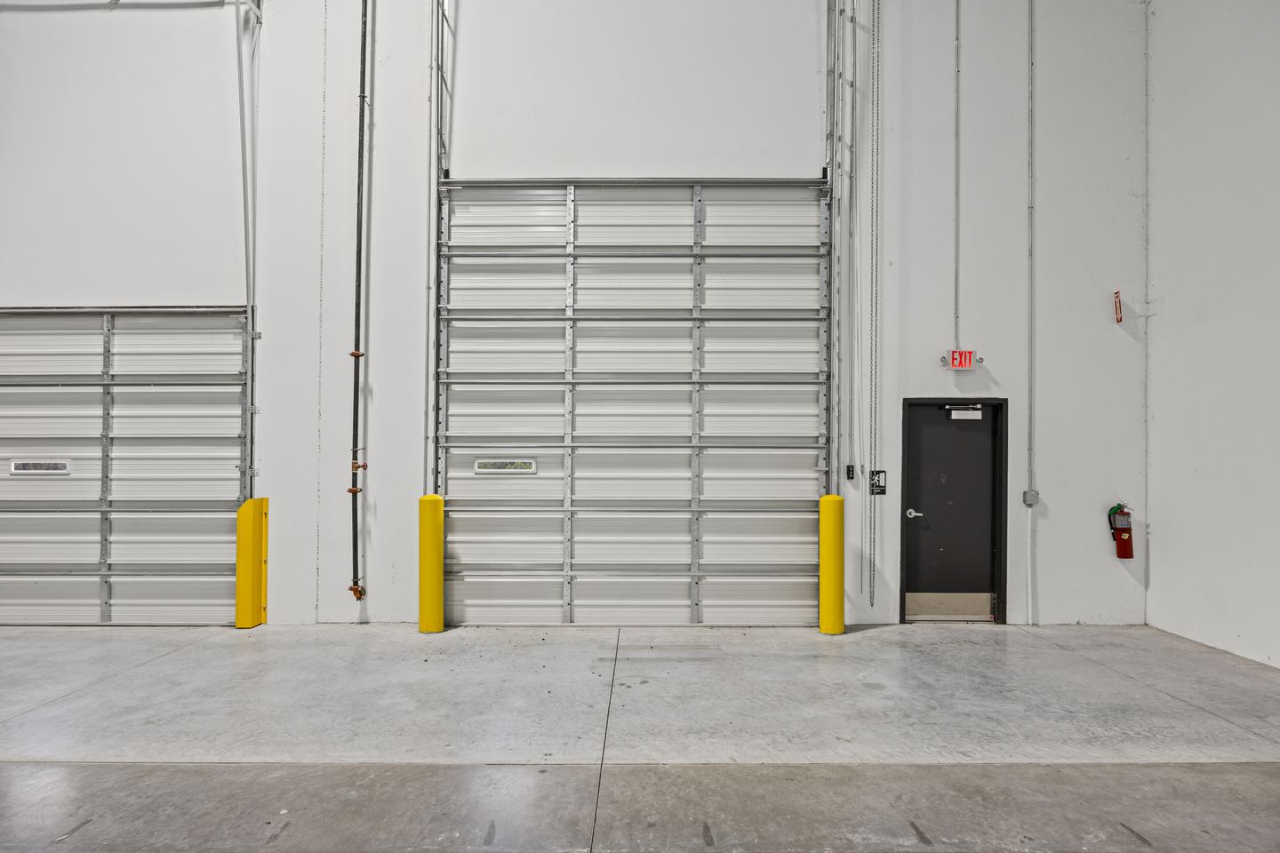 Two roll up dock doors with bollards and a steel personnel door between them