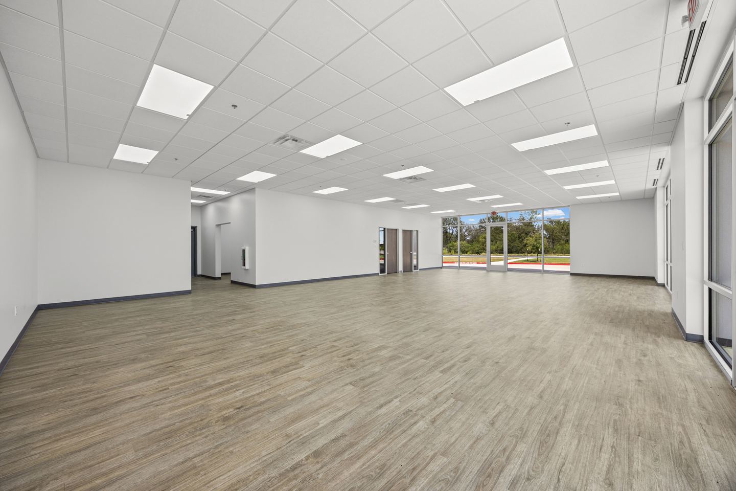 Open office floor with plank flooring, a grid ceiling and a wall of windows at the far end