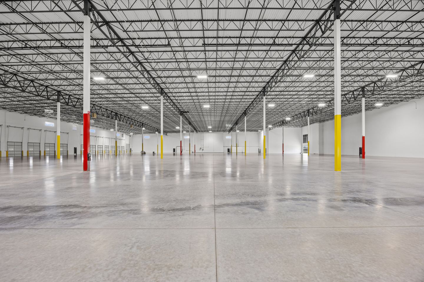 Empty warehouse floor with a polished concrete slab, red and yellow column guards and a steel truss roof
