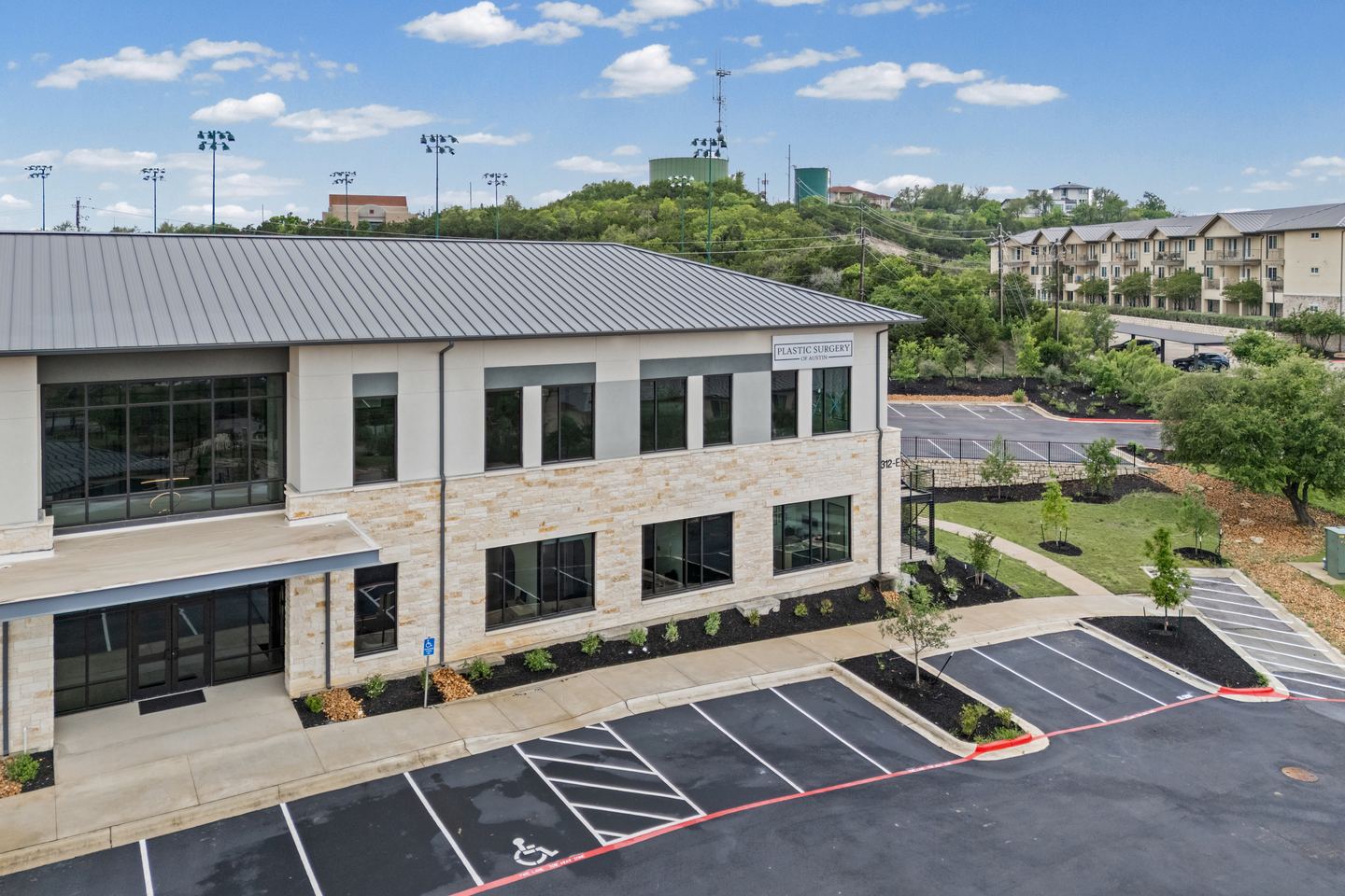 Two story limestone and glass medical office building with a metal roof, seen over the parking lot