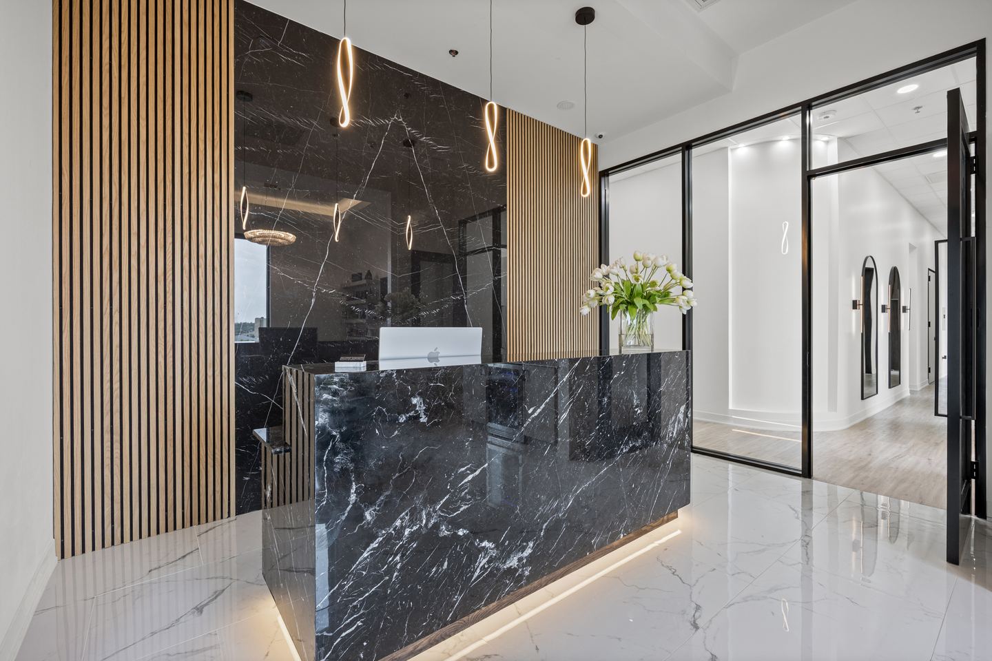 Plastic surgery clinic reception with a black marble desk, a timber slat wall and glass doors to the corridor