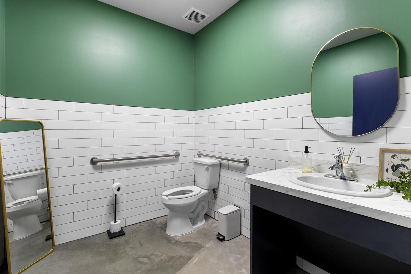 Client washroom with a green painted wall over white metro tile and a round mirror