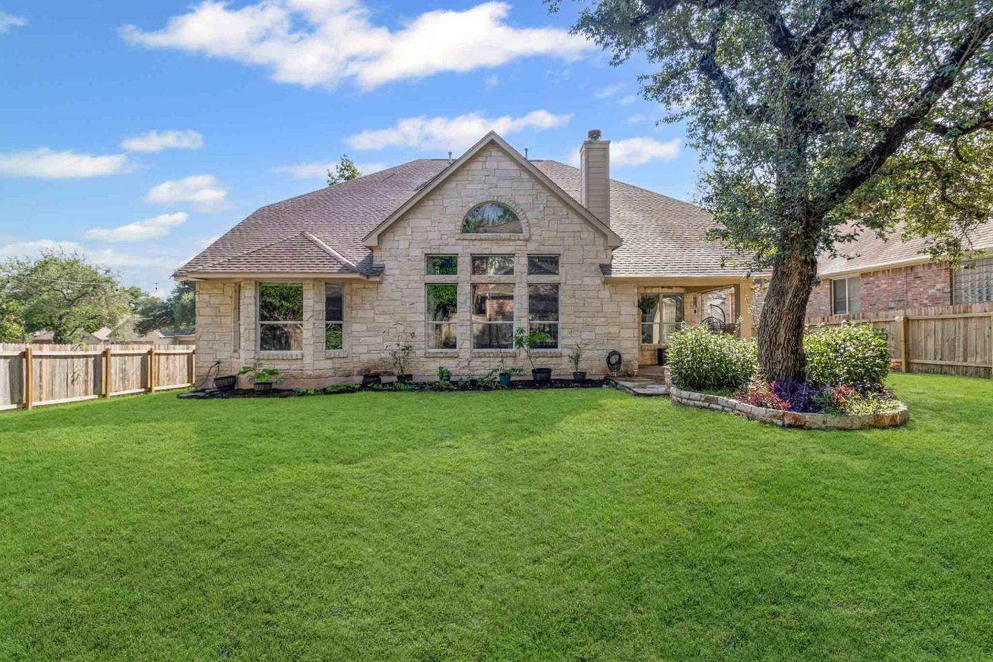 Stone home in Austin photographed across a large level lawn framed by a mature tree