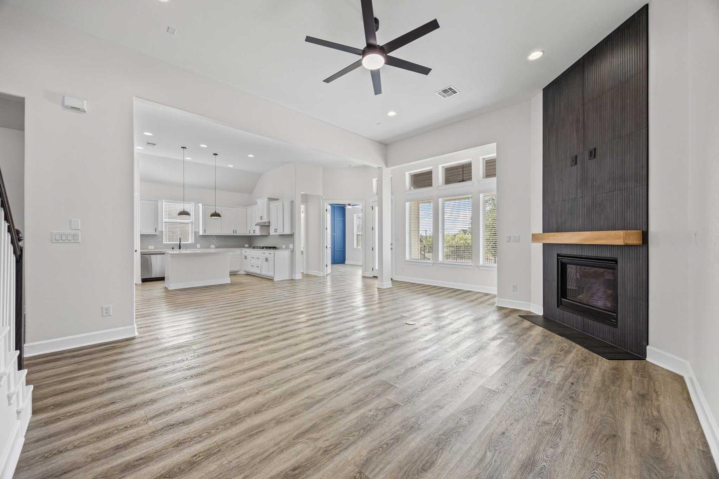 Vacant living room with a fireplace, tall windows and pale flooring before the owner moves in