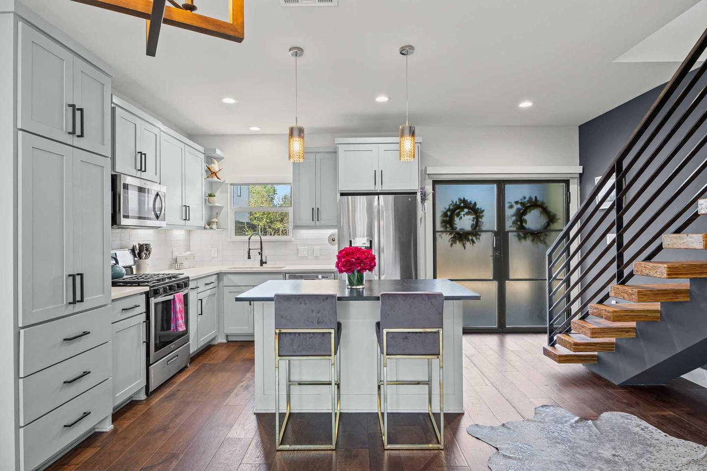 Short term rental kitchen in South Austin with a white island, bar stools and an open stair behind