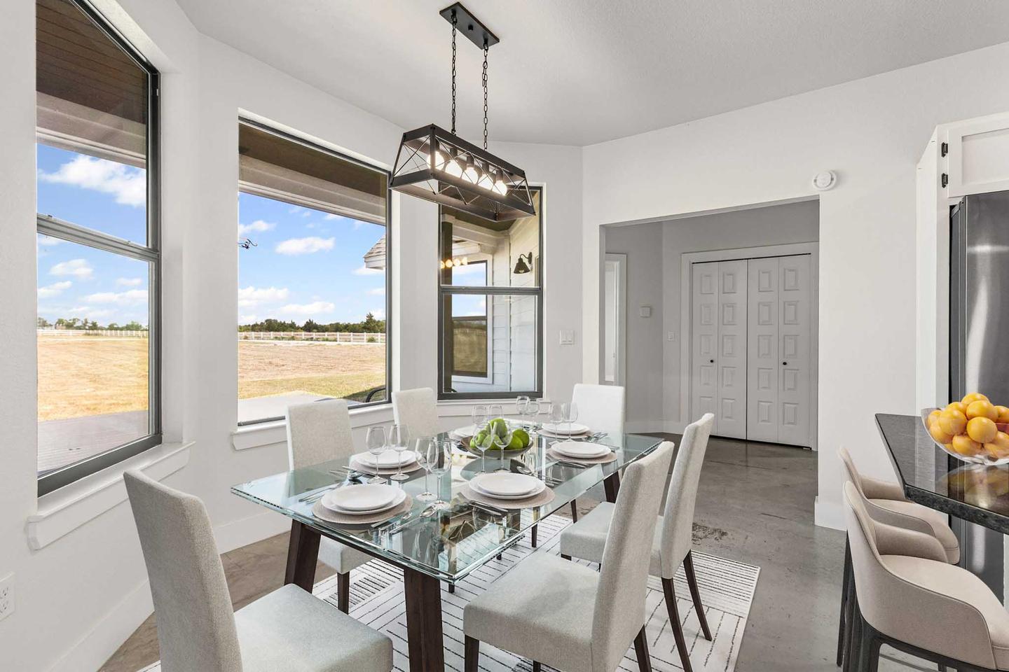 The same Manor dining area digitally staged with a glass table, white upholstered chairs and a linear pendant