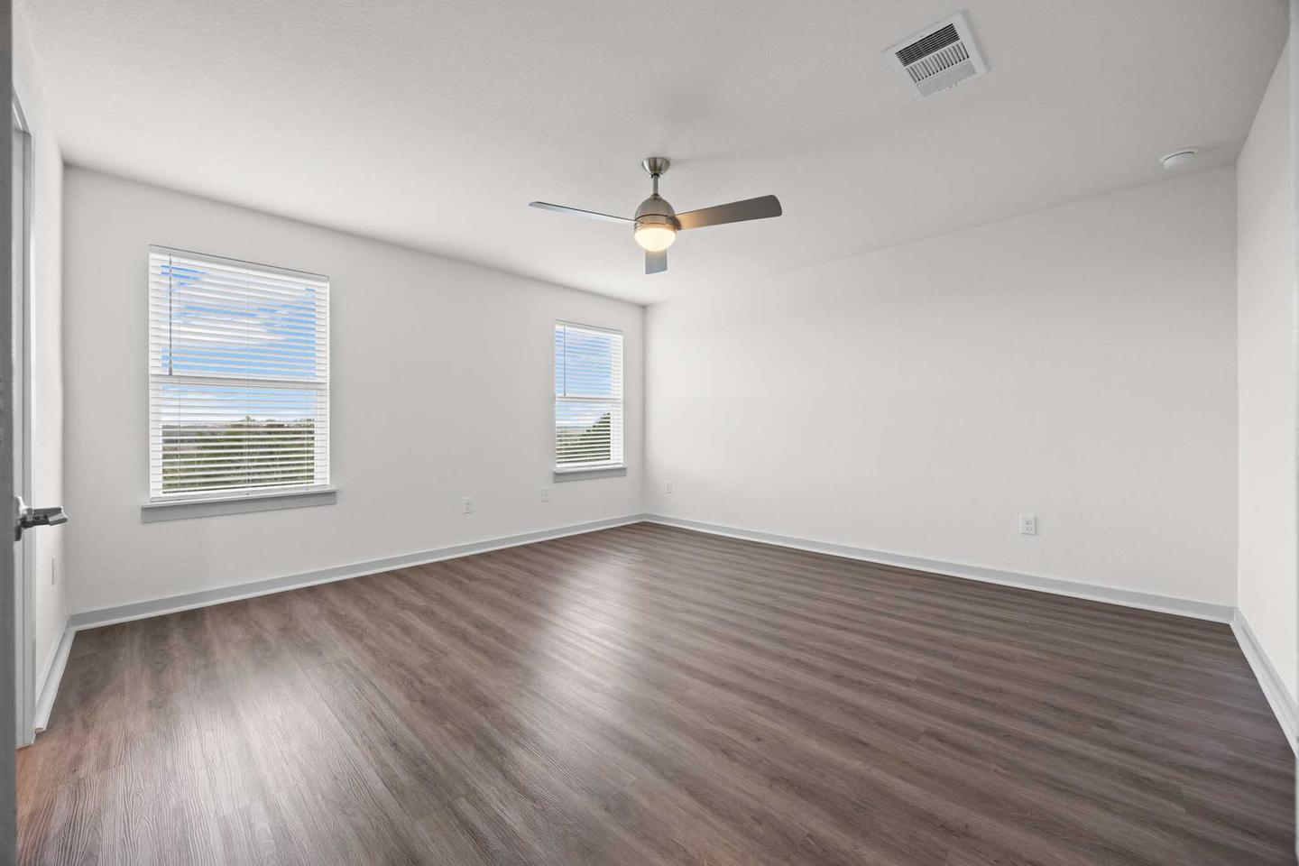 Empty bedroom in Pflugerville with bare timber flooring and two windows
