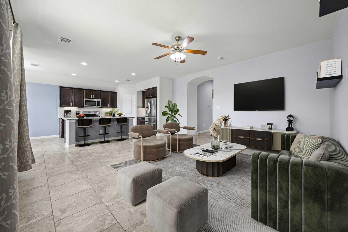 Living room digitally staged with a deep green sectional, a round ottoman and a wall mounted television