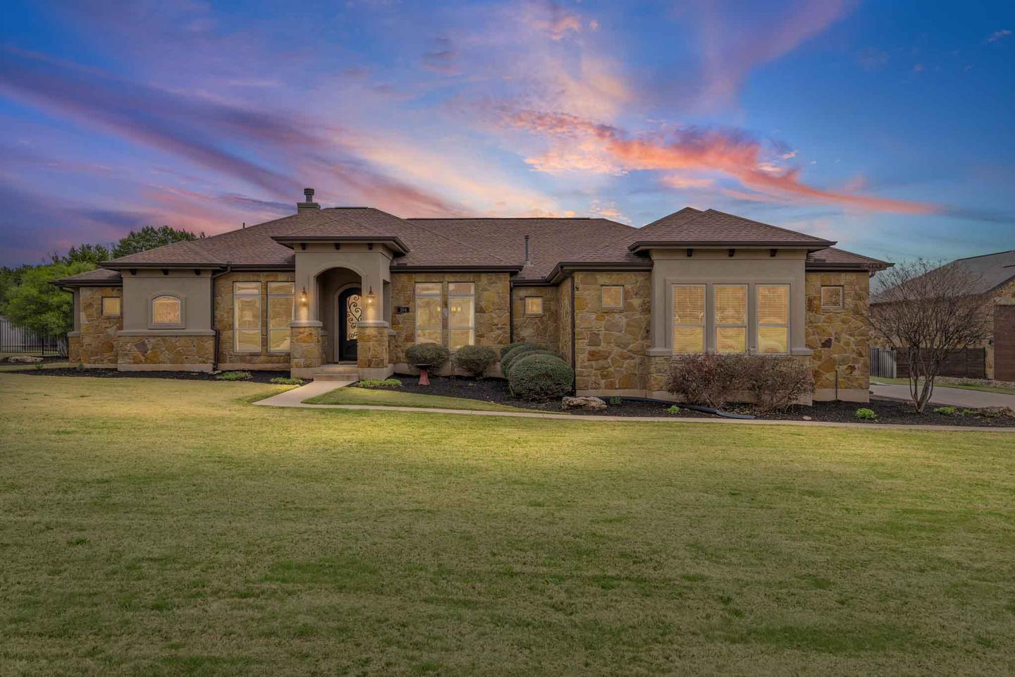 Single story stone home in West Austin at dusk with a violet sky and warm light in every window